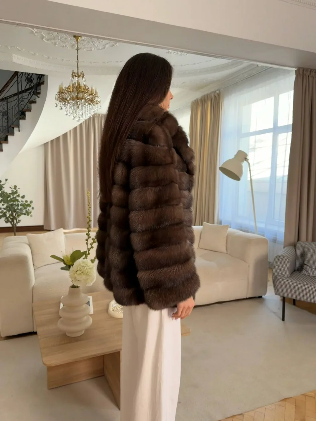 Modella di profilo in una giacca di zibellino in un salotto luminoso